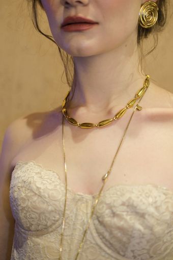 Colo de mulher com colar dourado de elos e corrente fina sobre vestido de renda creme