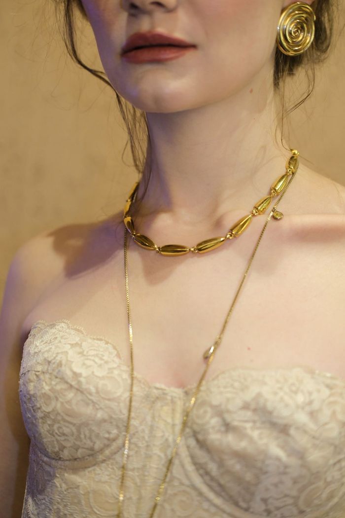 Colo de mulher com colar dourado de elos e corrente fina sobre vestido de renda creme