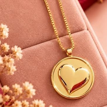 Colar da E.M com medalha dourada de coração em relevo e corrente veneziana, sobre estojo de veludo rosa