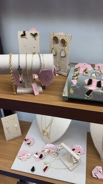 Expositor da E.M com colares em busto, brincos em cartelas rosa e peças sobre bandeja espelhada