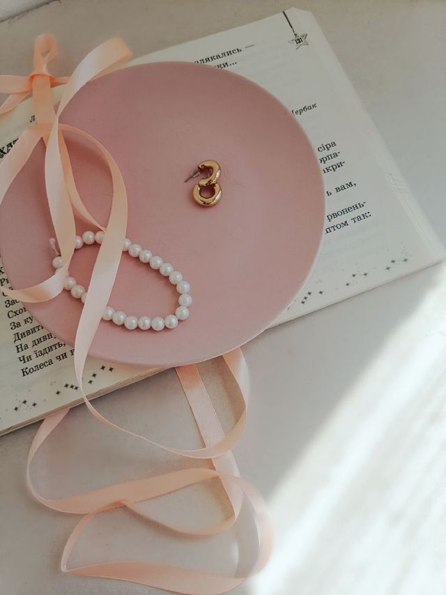 Pulseira de pérolas e brincos dourados em prato rosa com fita de cetim